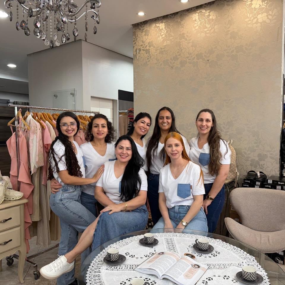 Equipe de consultoras da Regina Modas sorrindo dentro da loja, ao redor de uma mesa