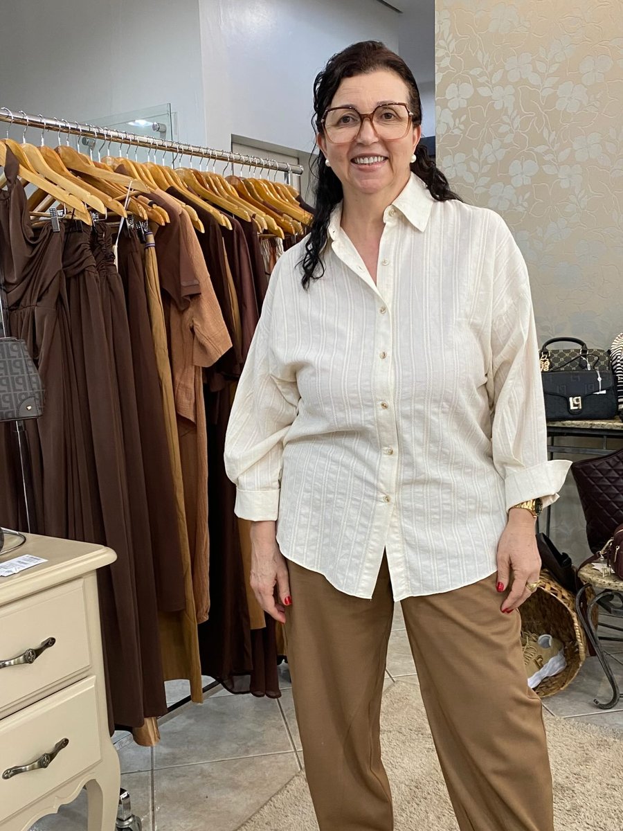 Look com camisa branca ampla e calça de alfaiataria caramelo, dentro da loja